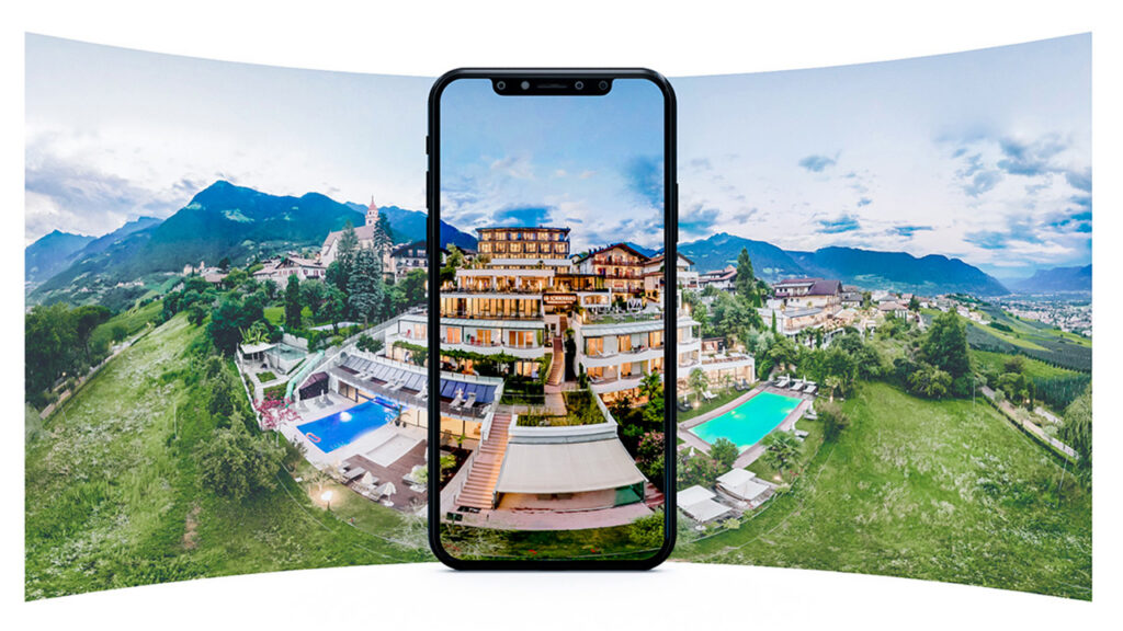 Smartphone zeigt eine interaktive 360‑Grad‑Ansicht eines Hotels in bergiger Landschaft