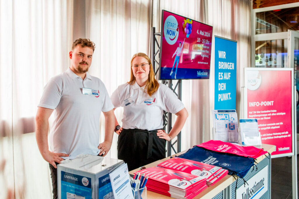 Zwei Personen stehen an einem Start Now Infostand.