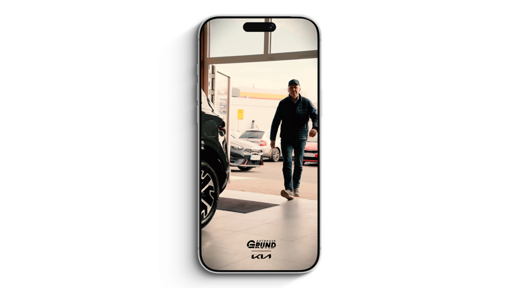 Smartphone‑Mockup mit Standbild Videoaufnahme: Person betritt einen Autohaus‑Showroom, im Bild ist das Logo Autohaus Grund / KIA sichtbar.