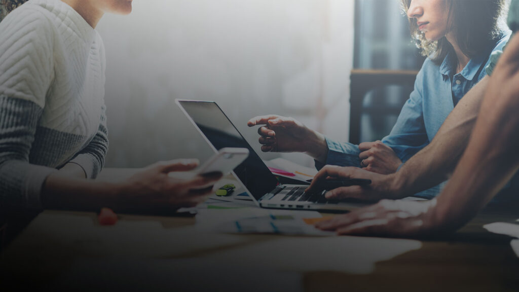Mehrere Personen arbeiten gemeinsam an einem Laptop und besprechen Inhalte am Tisch. ©AdobeStock