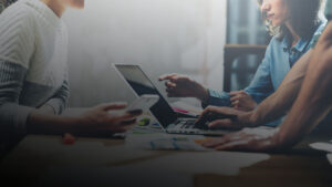 Mehrere Personen arbeiten gemeinsam an einem Laptop und besprechen Inhalte am Tisch. ©AdobeStock