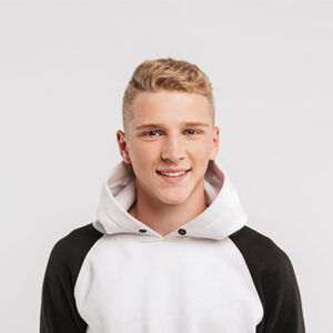 Porträt einer jungen Person mit kurzen hellen Haaren in einem weiß-schwarzen Kapuzenpullover vor einem hellgrauen Hintergrund. Die Person blickt direkt in die Kamera. ©AdobeStock