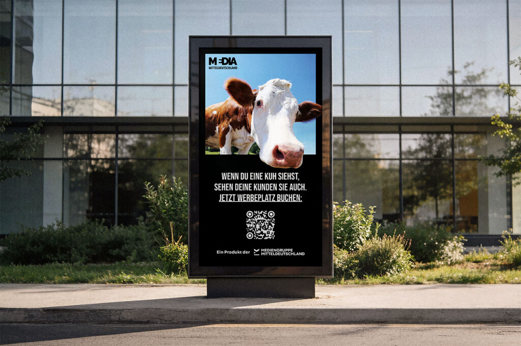 Digitale Werbestele vor einem Bürogebäude mit einer Kuh und QR-Code auf dem Display. ©Mockup AdobeStock, Inhalt Mediengruppe Mitteldeutschland