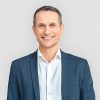 Professionelles Porträt einer Person in blauem Business-Sakko und weißem Hemd vor neutralem Hintergrund. Die Aufnahme vermittelt einen seriösen und professionellen Eindruck. ©AdobeStock